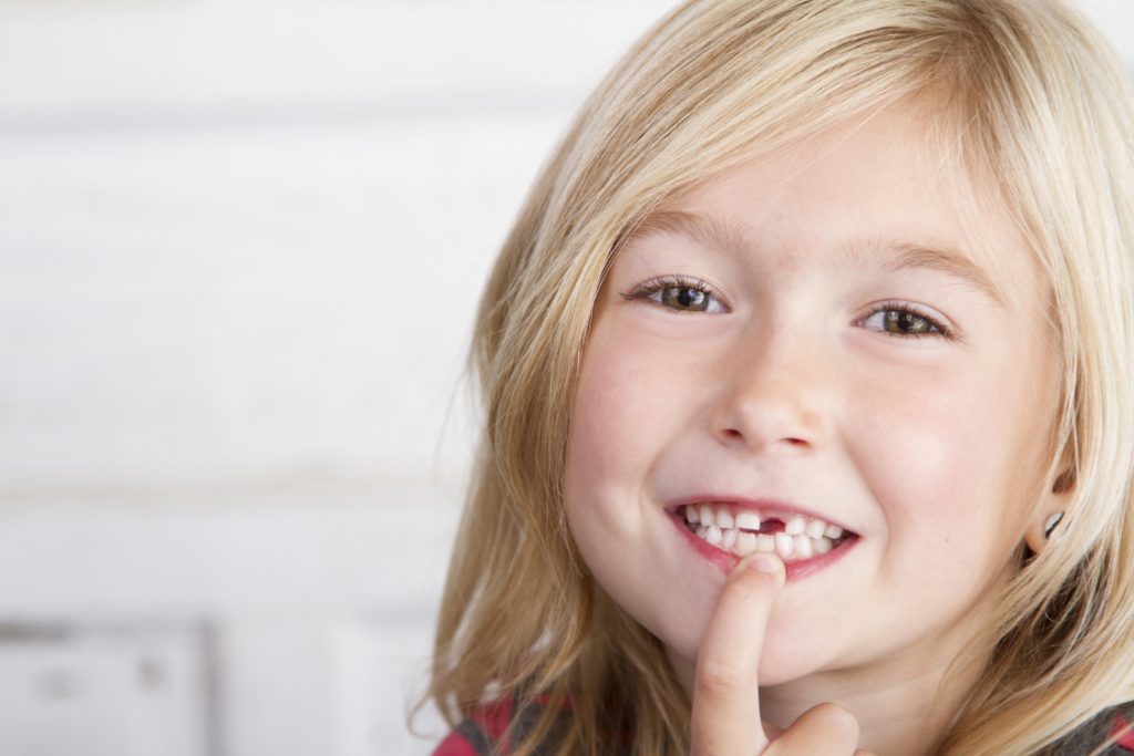 Child missing front tooth pointing at it with her finger