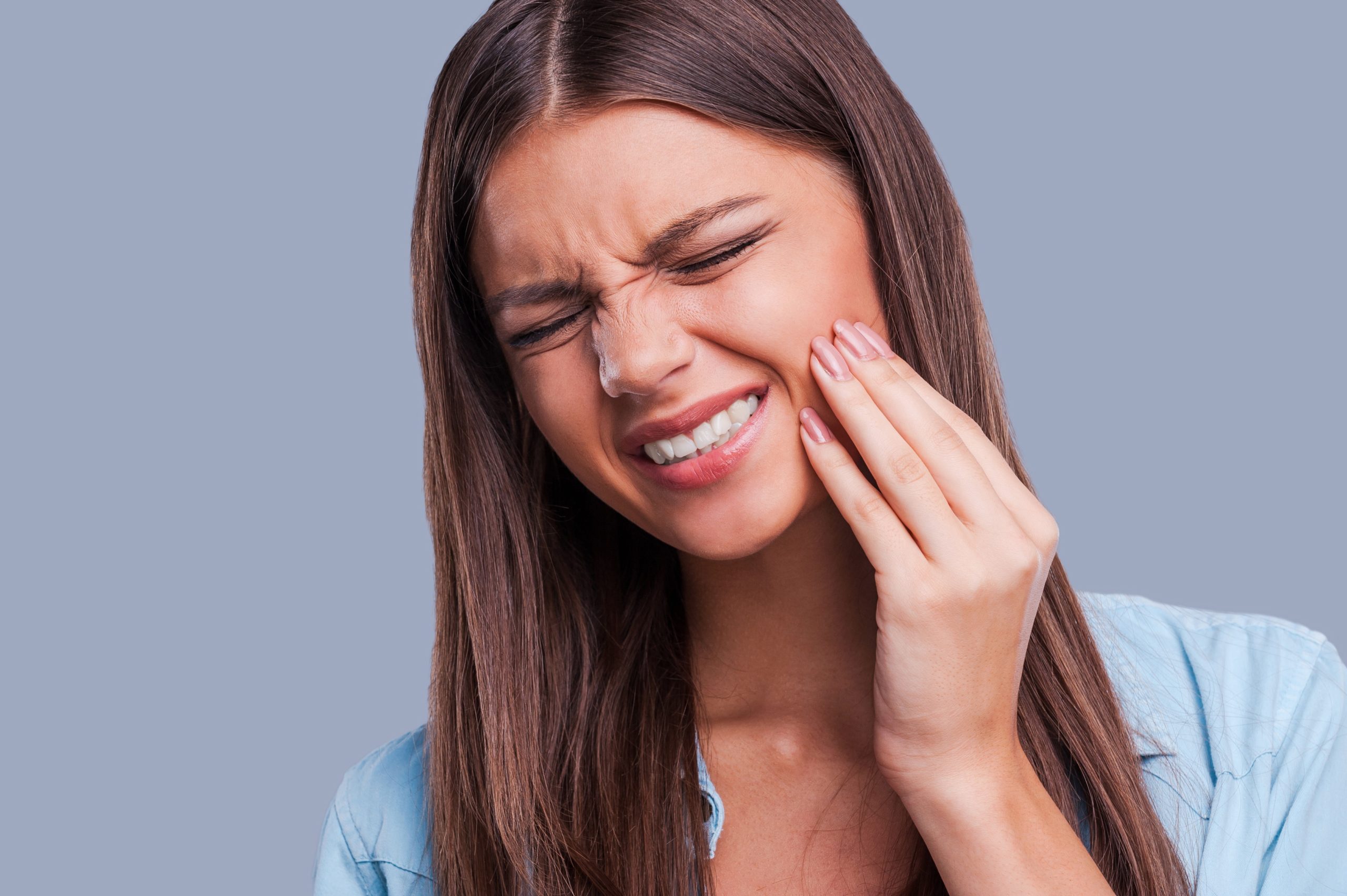 Young woman suffering from toothache while standing against grey background